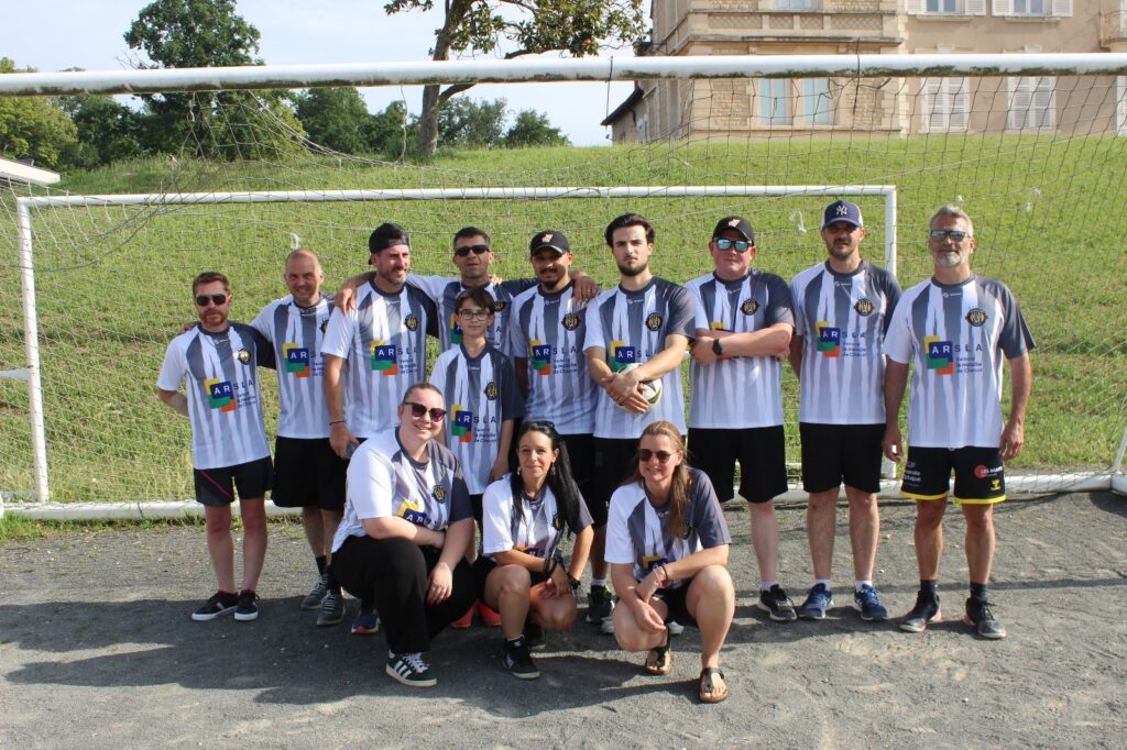 Groupe de personnes en maillots de football devant un but en extérieur.