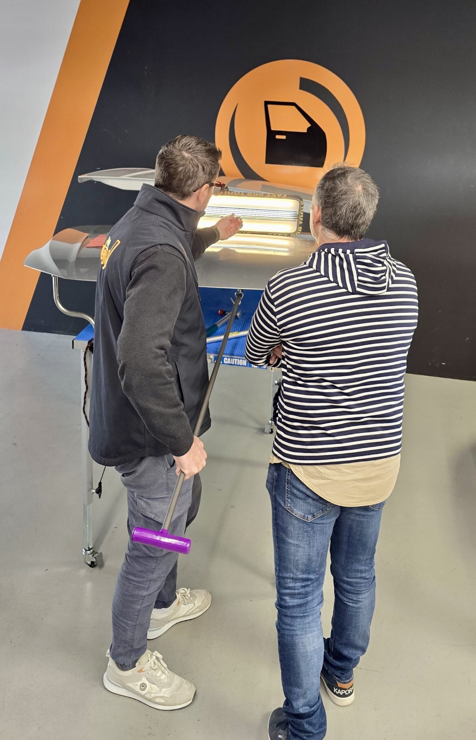 Deux hommes regardant une démonstration de manette de jeu vidéo sous une signalisation