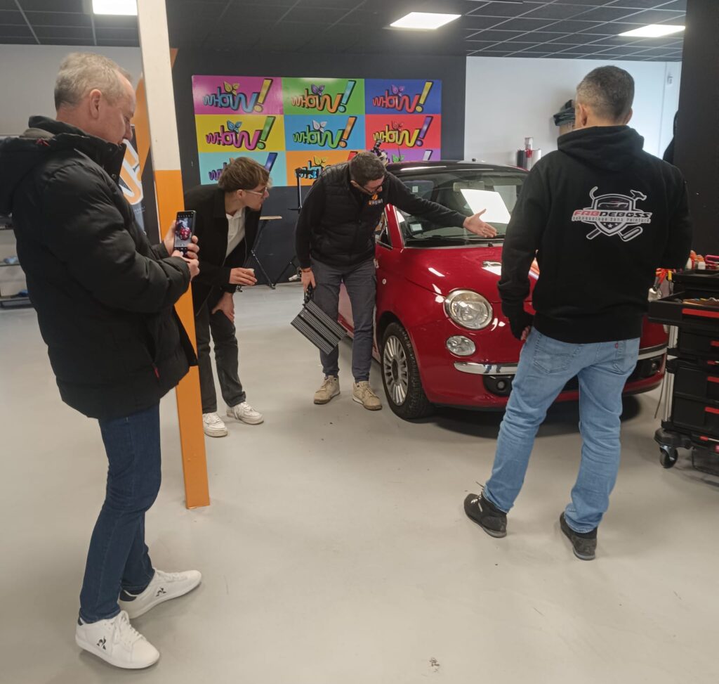 Groupe de personnes examinant une petite voiture rouge dans un atelier