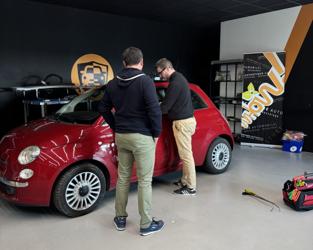 Deux hommes travaillant sur une petite voiture rouge dans un garage.