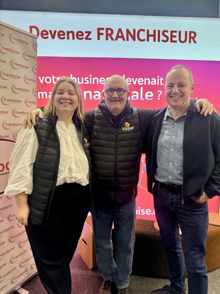 Trois personnes souriantes posent ensemble devant un écran rouge avec texte.