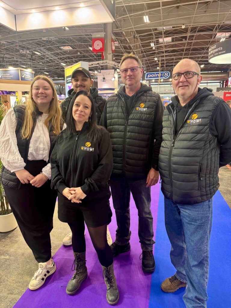 Groupe de quatre personnes portant des vestes avec logo, dans un salon d'exposition.