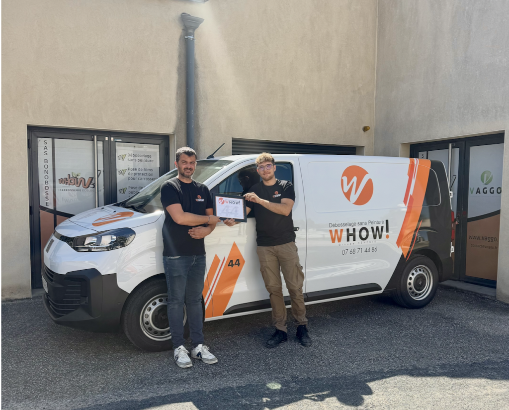 Deux hommes posent devant une camionnette blanche avec logo et texte publicitaire.